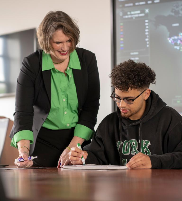 A cybersecurity professor talking with a student. A threat map is in the background.