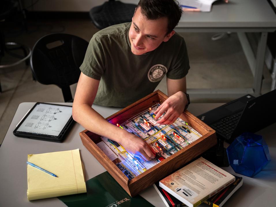 A student in the computer science lab works with circuits and sits at a desk covered with notes and an iPad.