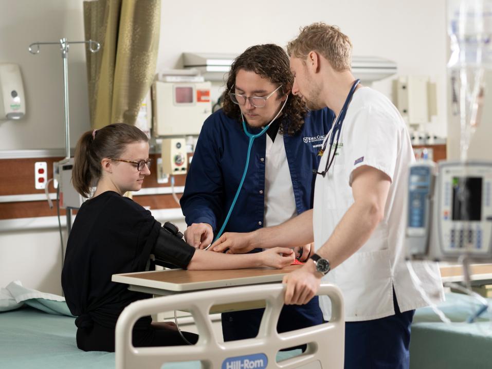 Two nursing students checking the pulse of student patient in the nursing lab.