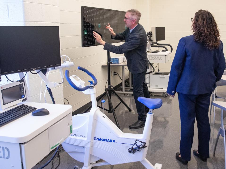 An equipment cart, a stationary bike, and a touch screen are visible in the Exercise Science Lab at York College as instructors demonstrate the analysis tools.