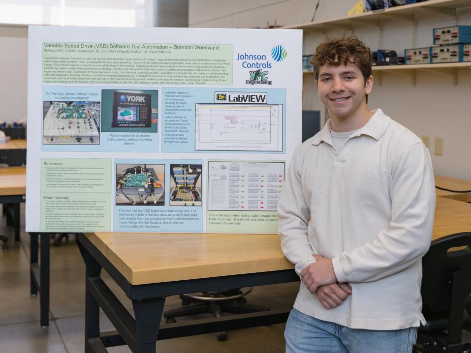 A student stands next to his poster presentation in a classroom.