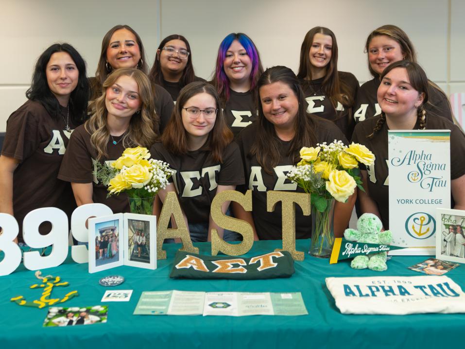 A group of sorority sisters posing at a table in front of their Greek Letters.