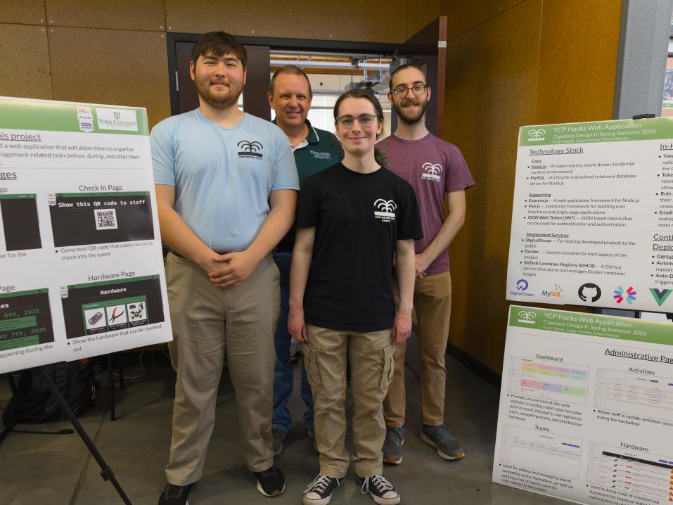 York College of Pennsylvania students and a faculty member pose beside project posters showcasing a web application developed for YCP Hacks.
