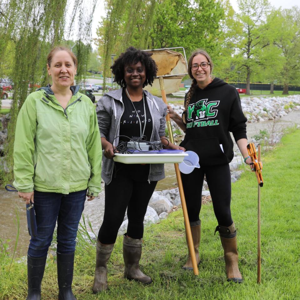 Three students pose in front of creek with clean up gear