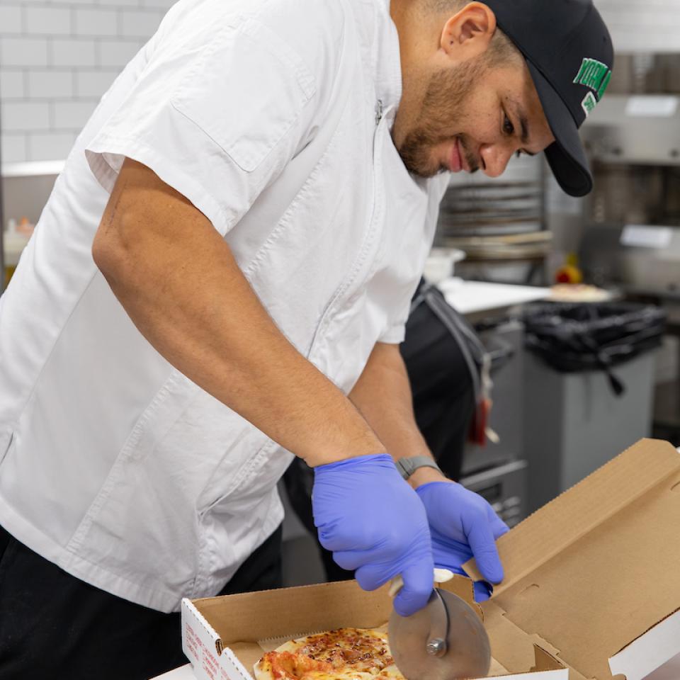 Chef Hector cuts a pizza pie in a to-go box.