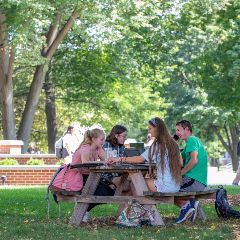 A group of four students study outside at a picnic table on campus.