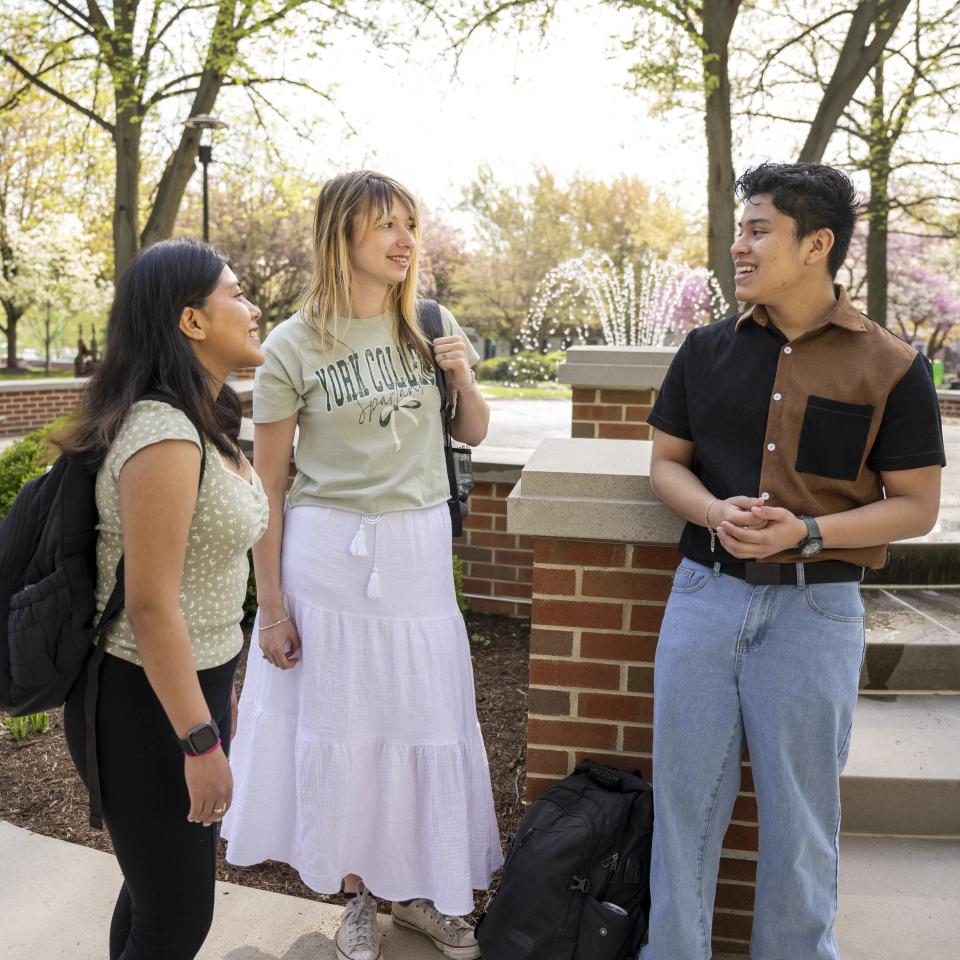 Three students talk near the fountain