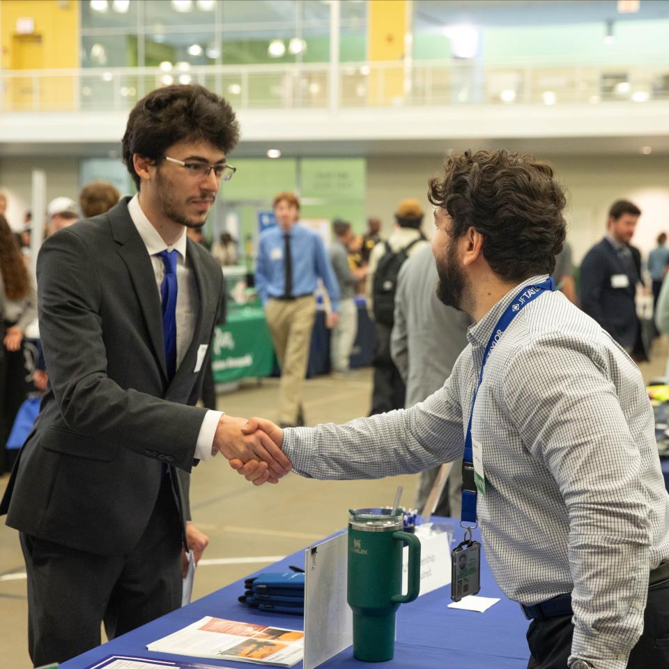 Two people in business attire shake hands at a networking event.