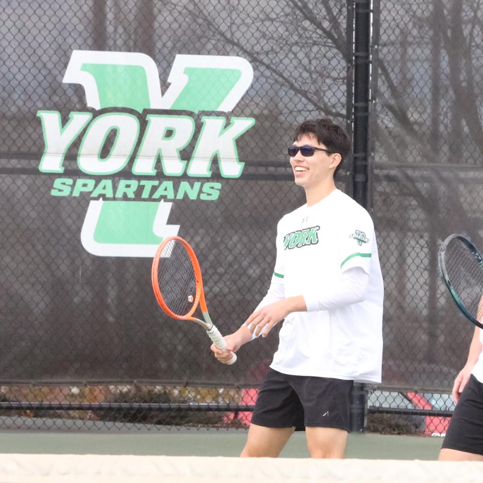 YCP Men's Tennis players on the court with a large York logo behind them.