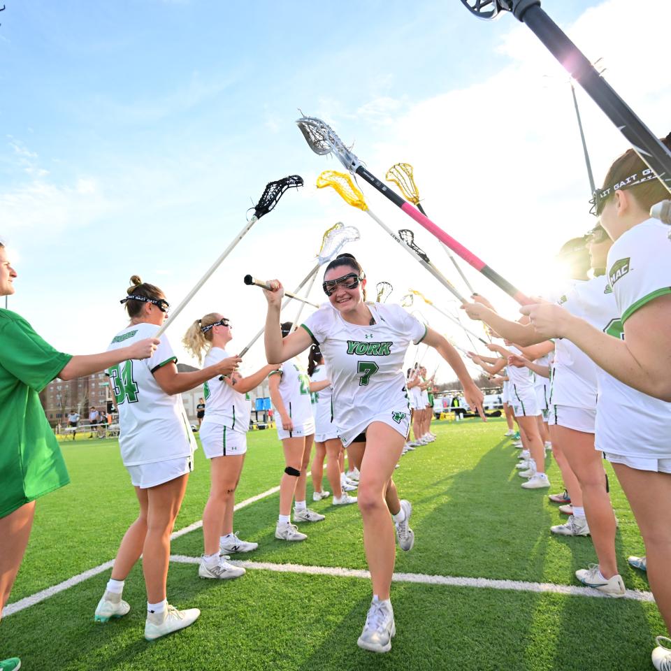 YCP Women's Lacrosse players hold up their sticks while a player runs through the middle.