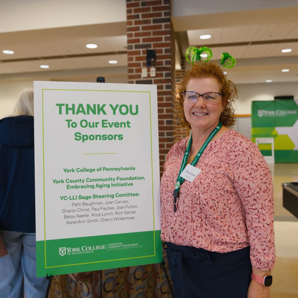 A woman stands next to a sign that reads, "Thank You to our event sponsors"