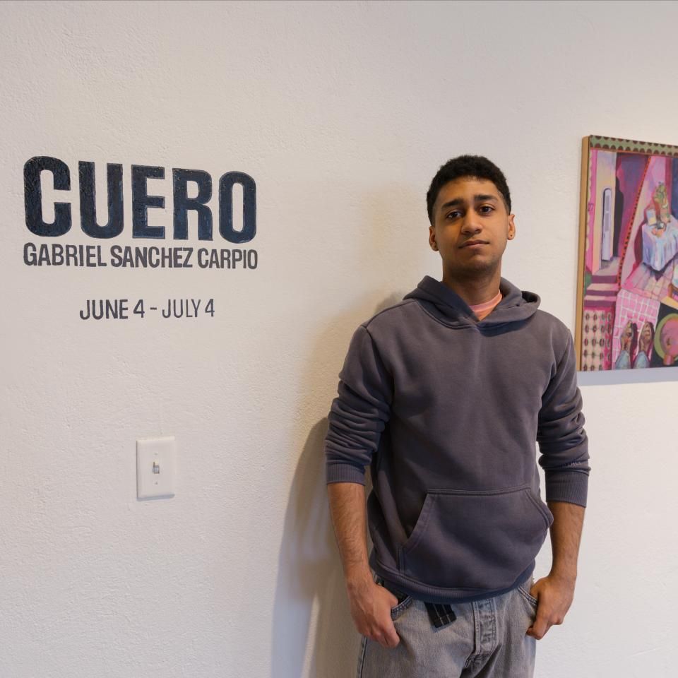 Gabriel Sanchez Carpio standing next to his name and his art show Cuero with the dates and a painting behind him.