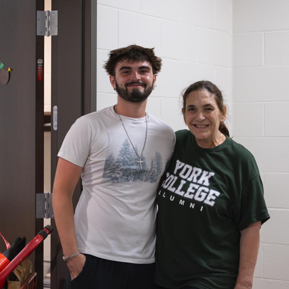 A mother and son pose outside his dorm room.