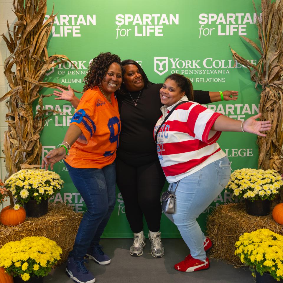 Three women stand together in front of a fall photo wall set up.