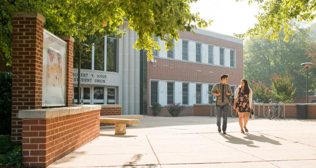 Two students walking outside on a sunny day in front of a red brick building