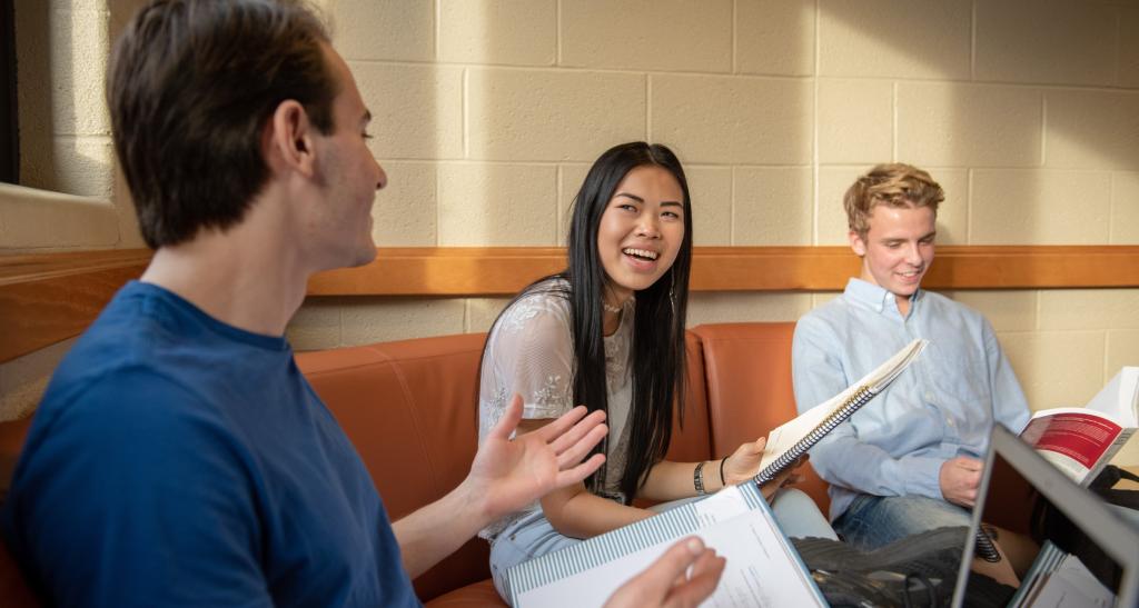 Three students sitting on a couch, laughing and studying together.