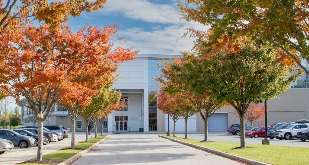 Trees with orange and red foliage line the sidewalk leading up to the Grumbacher Center.