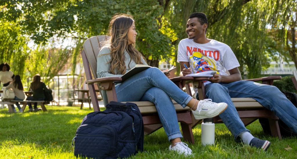 Two students sitting outside in chairs studying