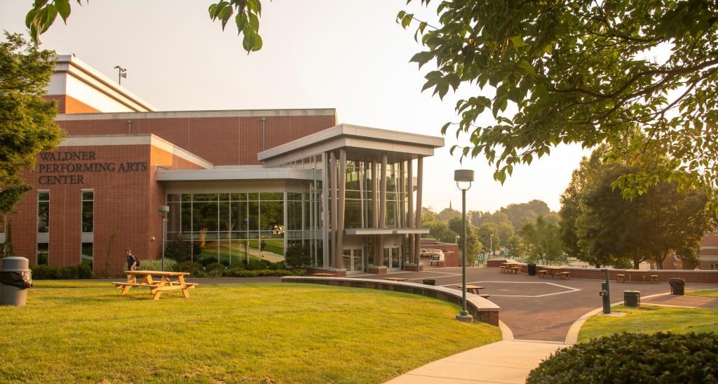 An exterior view of the Performing Arts Center at sunset. The building is brick with an ornate glass front.