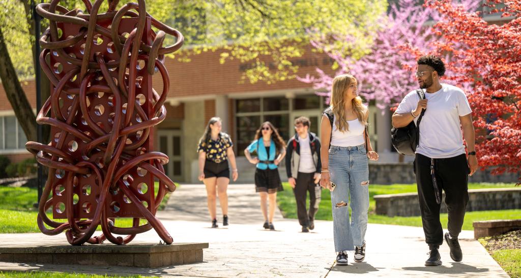 Students walking on main campus past a dark red metallic sculpture