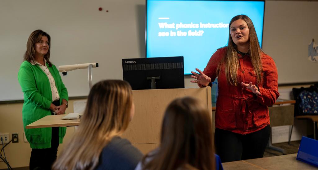 A student teacher lectures in front of a class; the podium is behind her.