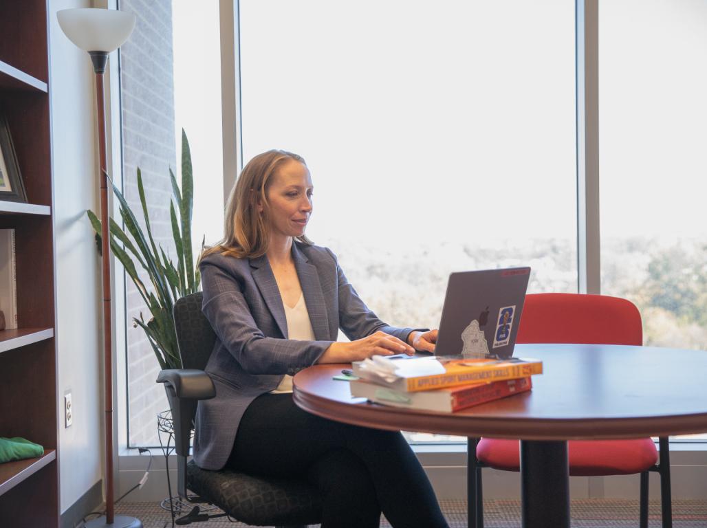 Molly Sauder works on her laptop at a small round table in her office.