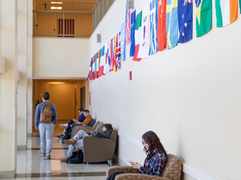 Students sitting in the chairs against the wall with flags from all over the world.