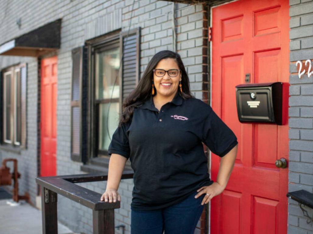 Portrait of AliceAnne Frost standing in front of a building made of gray brick with two bright red doors.