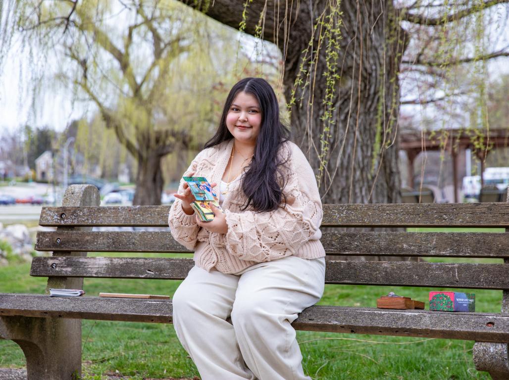 Malika sitting on a bench next to the Tyler Run Creek with her tarot cards.