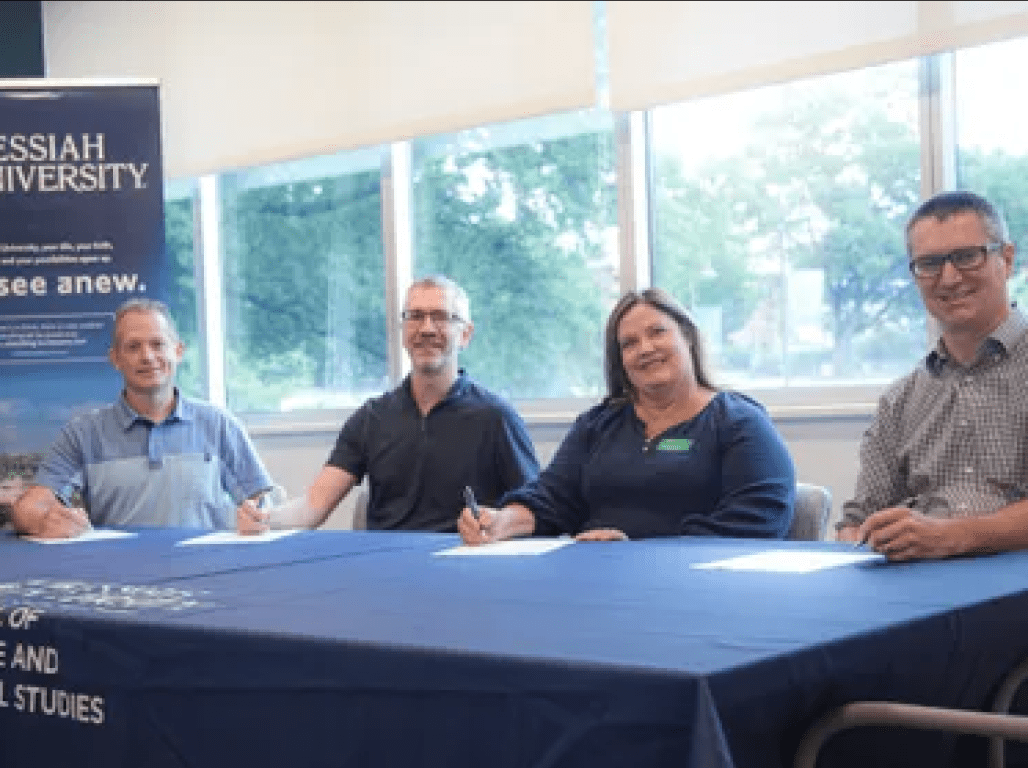 Four representatives from York College and Messiah University gather at a table for the signing event at Messiah.