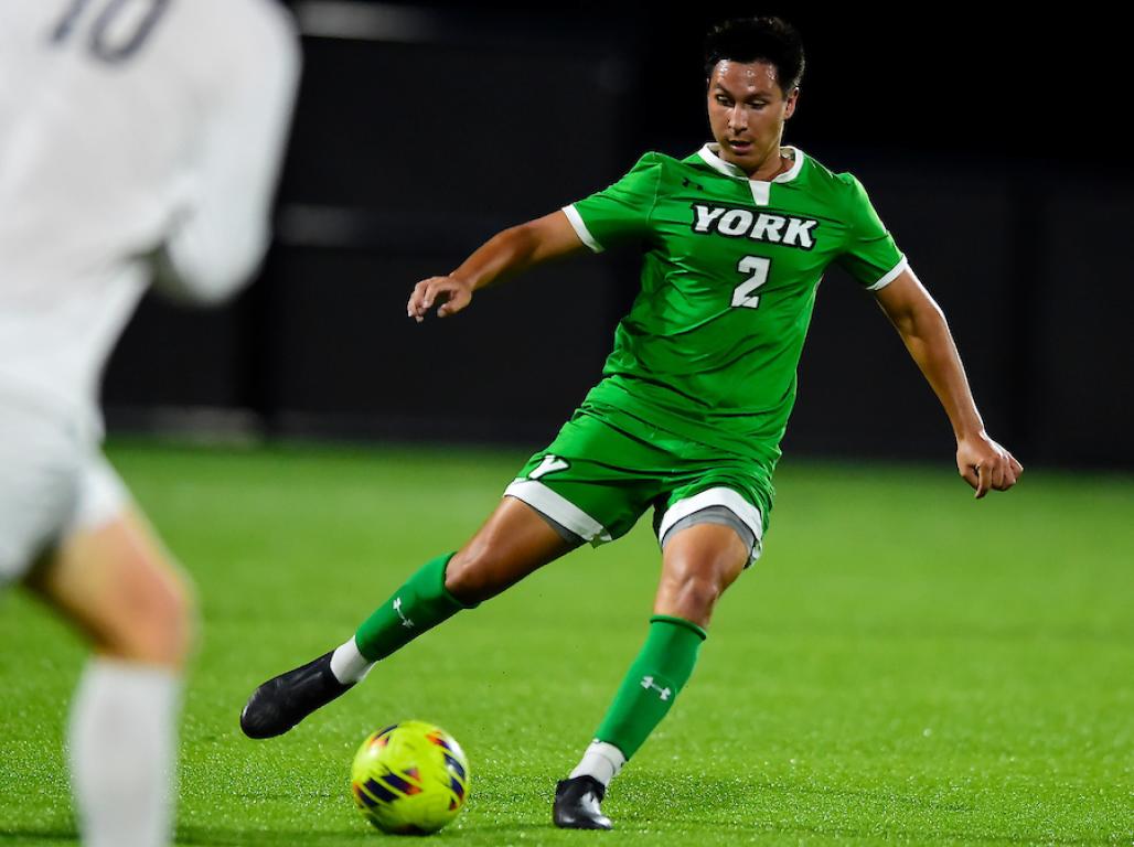 A Men's Soccer player kicking the yellow soccer ball with his right foot.