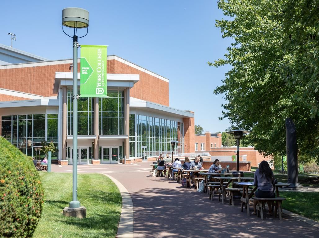 Students sit at picnic tables lining the sidewalk in front of the Performing Arts Center at York College.