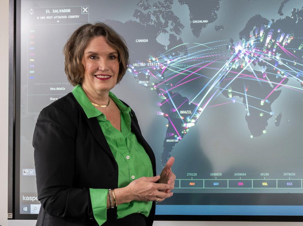 Dr. Tammy Schwartz lectures in front of her class, standing by a large smart screen with a cybersecurity map displayed.
