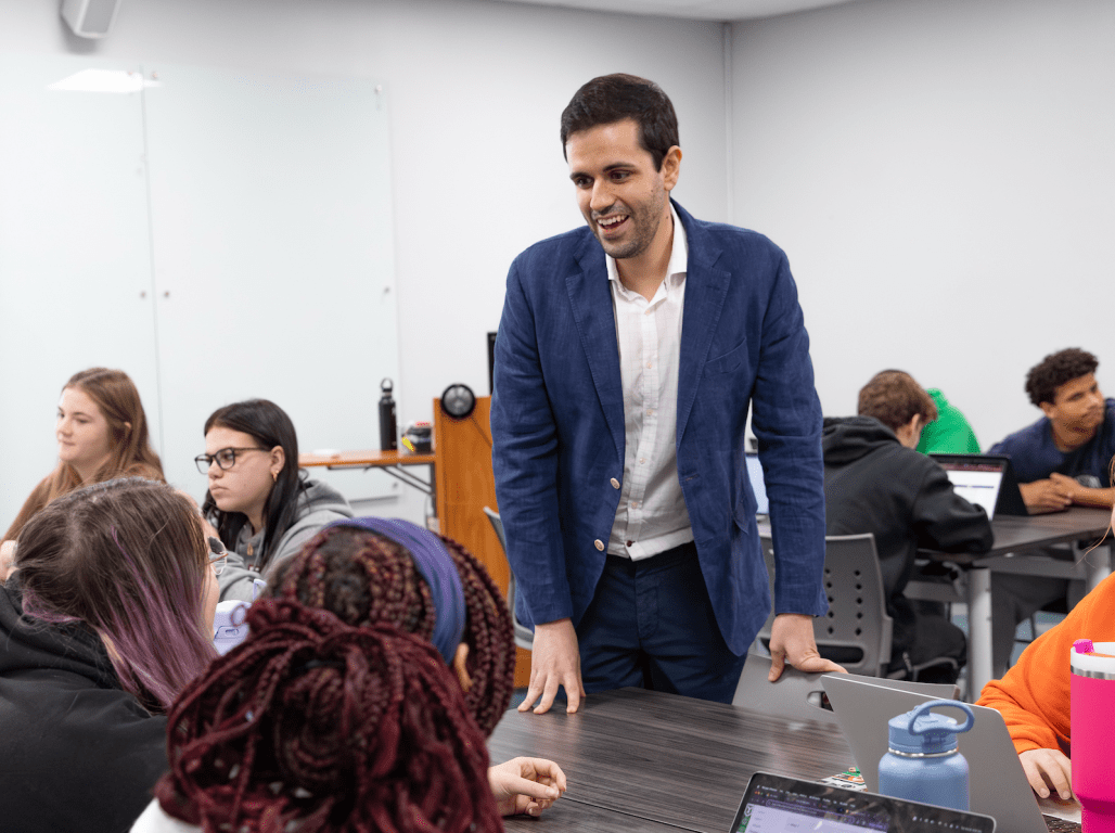 Dr. José Luis de Ramón Ruiz talks to a group of students seated around a table in his classroom.