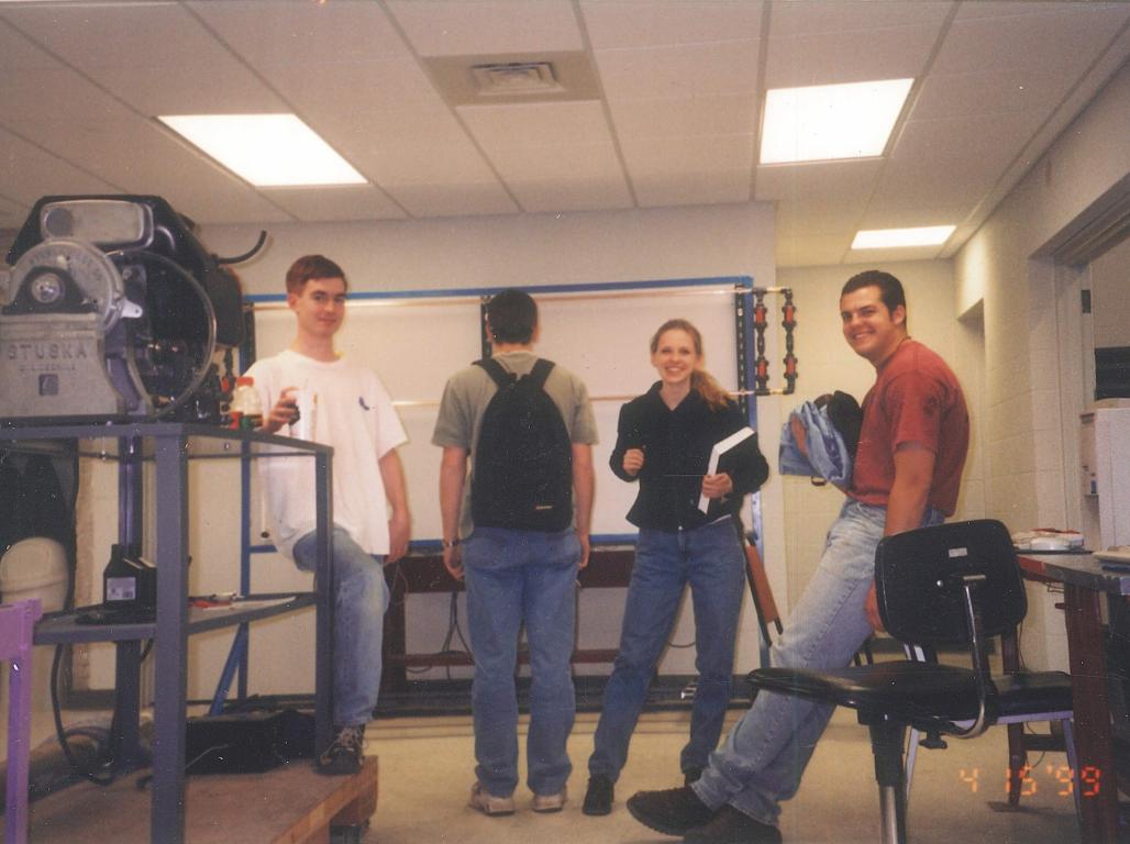 A vintage photo from the 1990s shows four college students hanging out in an engineering lab classroom.