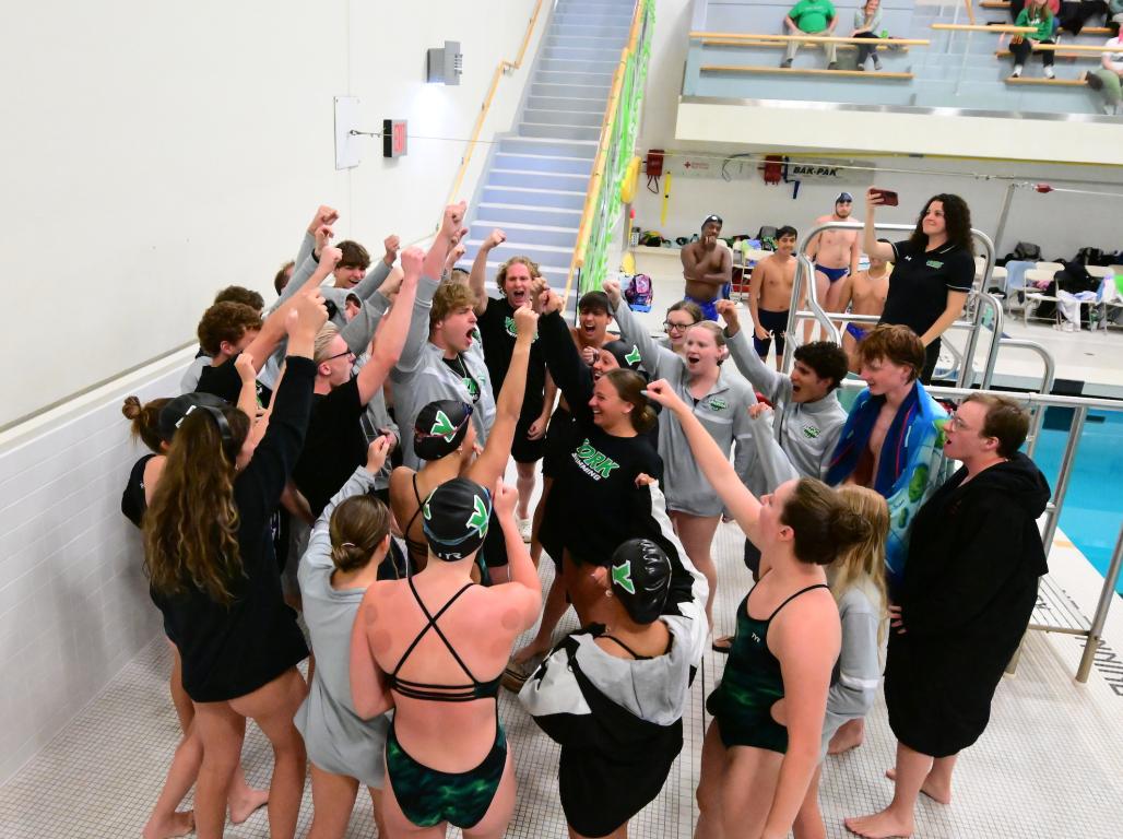 Members of the York College swim team celebrate with arms raised by the pool.