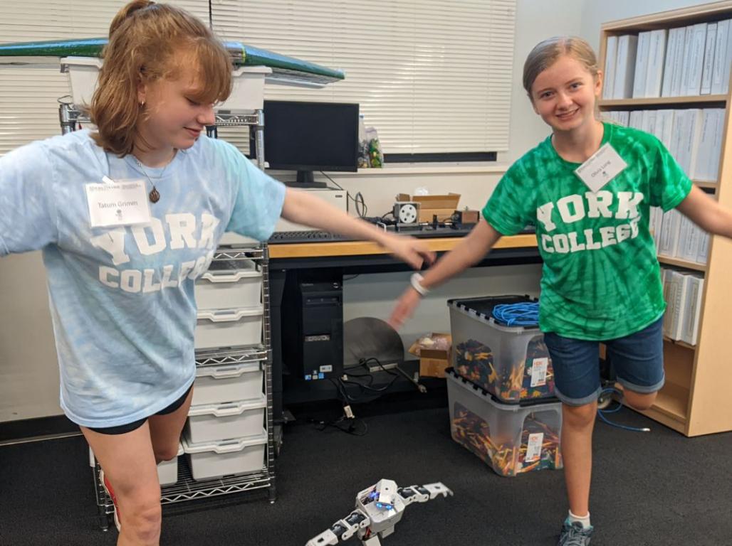 Two students mimic a robot's pose during a robotics class.