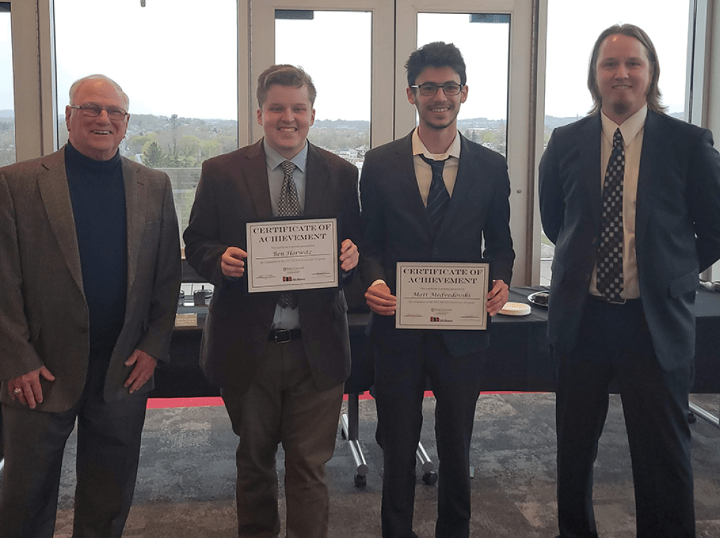 Four people smiling at the camera, two of them holding certificates