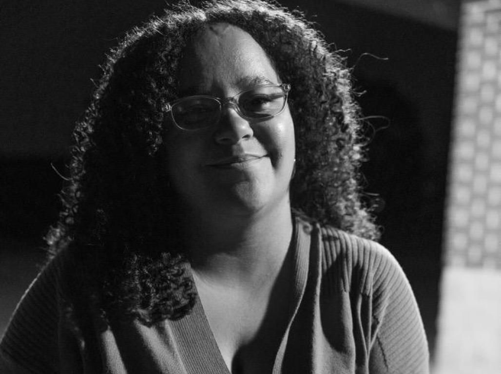 B & W portrait of Akira Camacho-Romero holding a camera.