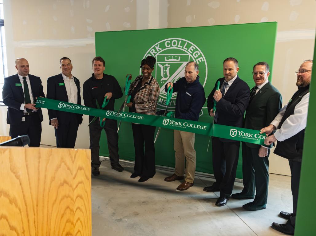 A group of individuals ceremoniously cutting a green ribbon at an event.