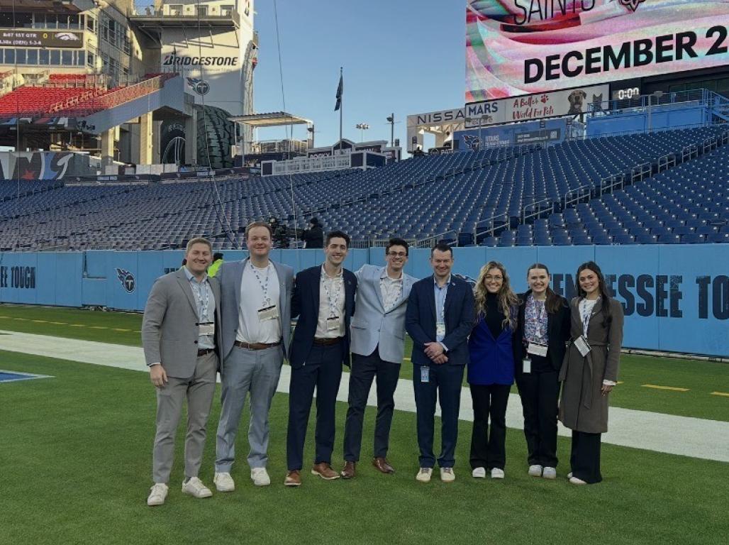 A group of people in business attire posing on the field at the Tennessee Titans stadium.