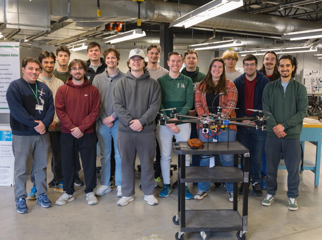 A group of engineering students smiling at the camera with a large drone positioned on a cart in front of them.