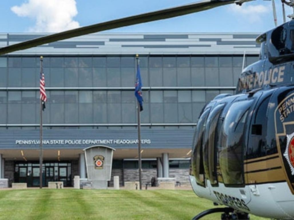 A helicopter is seen in close up with the Pennsylvania State Police Headquarters building in the background.
