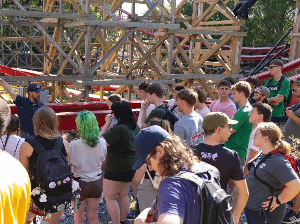 York College Civil Engineering students gather beside a roller coaster while learning about its structure and engineering systems.
