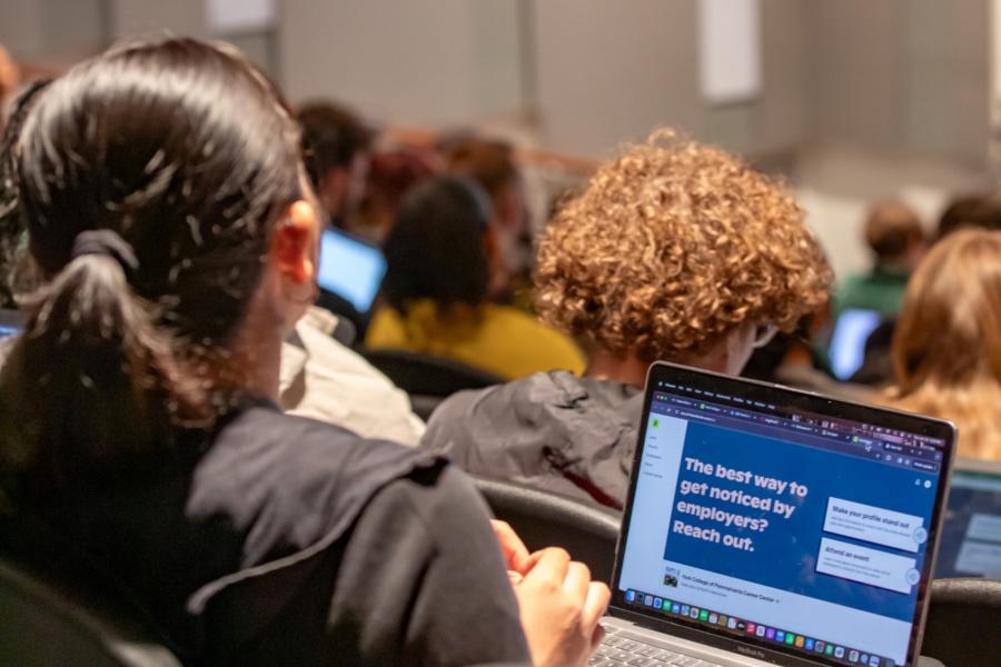 A student sits facing away from the camera in lecture hall with a laptop open.