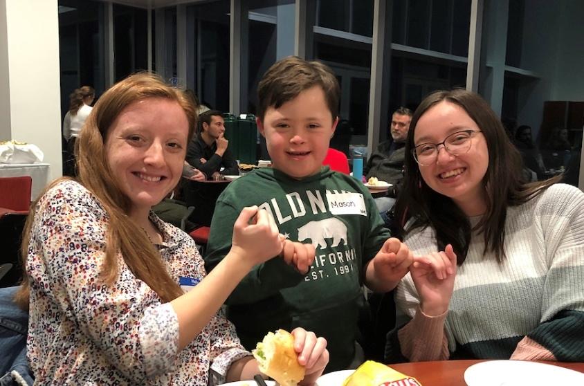 Two students pose holding hands with a child between them.