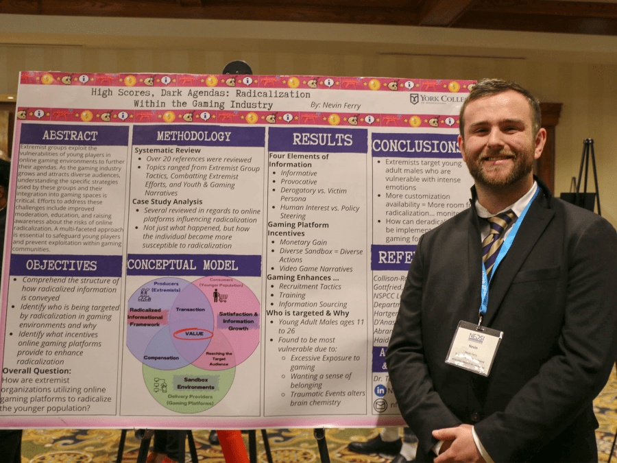 Student smiling at the camera in front of a research poster titled "High Scores, Dark Ages: Radicalization Within the Gaming Industry."