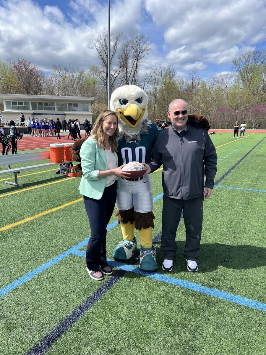 Jessica Huntley posing with a football, an eagle mascot, and another person, smiling at the camera. 