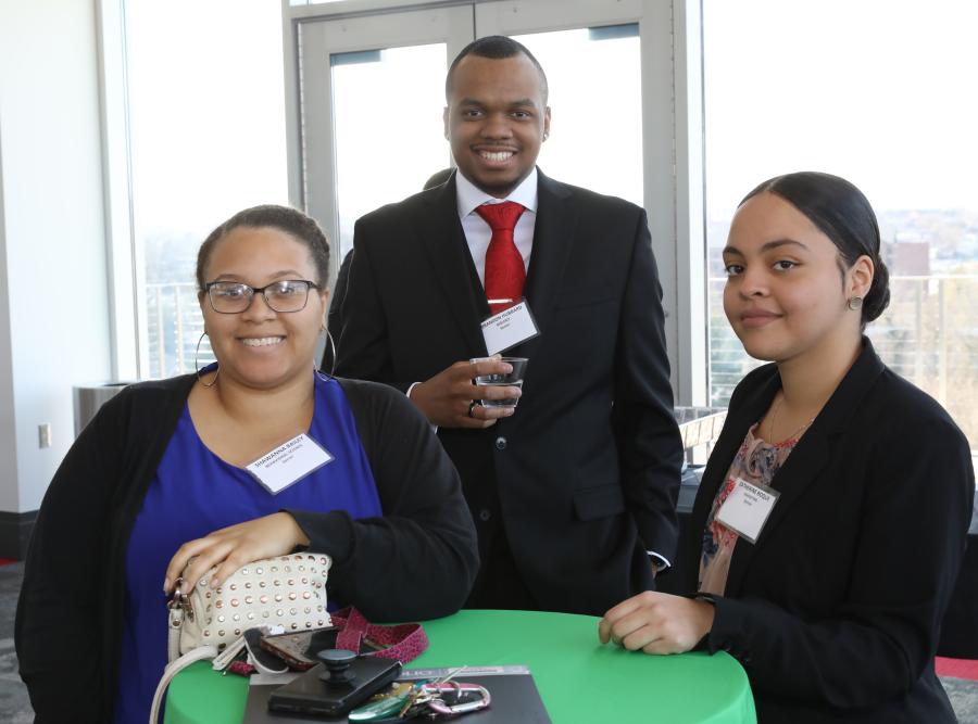 Three individuals in business attire pose for a photo in a sunlit room.