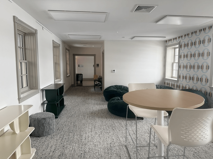 An empty room with windows, tables, chairs, and bean bag chairs.